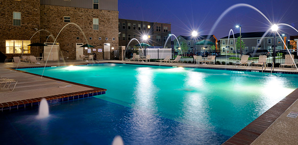 The pool at Harmony Oaks in the evening, with the pool lights and fountains lighting up the water.